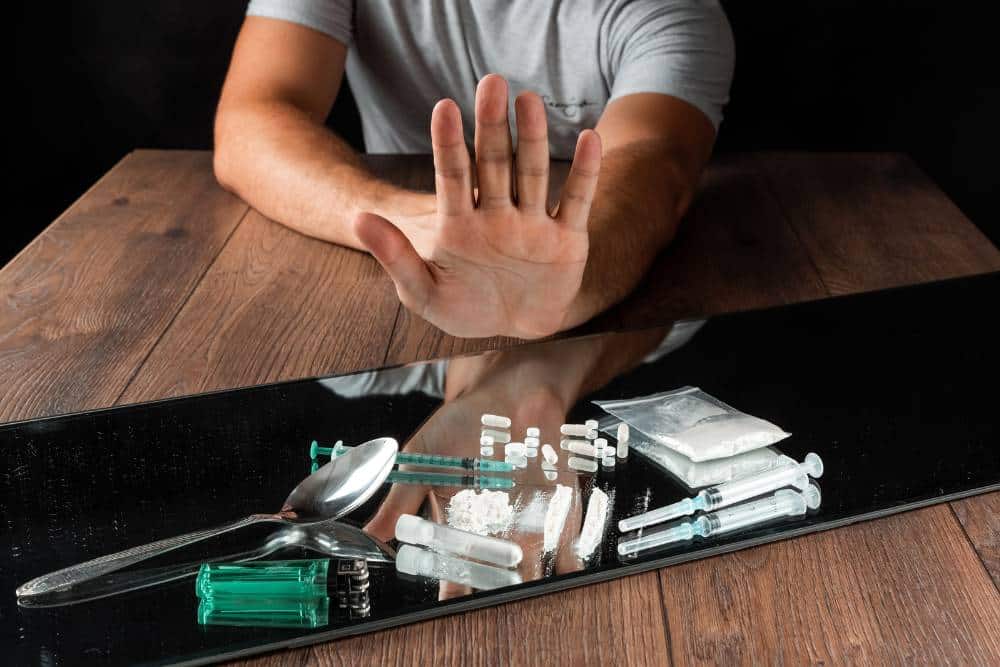 A person making a stop gesture towards heroin and drug paraphernalia on a table, symbolizing heroin addiction treatment in Huntington Beach CA.