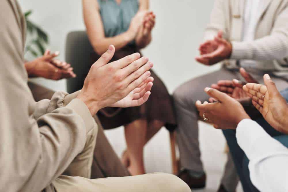 Close-up of group therapy participants clapping in support during a Heroin Addiction Treatment in Huntington Beach CA session.

