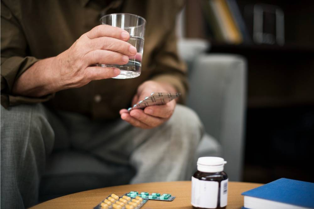 Close-up of a person holding a glass of water and blister pack of prescription pills, illustrating the struggle before prescription drugs addiction treatment in Huntington Beach, CA.