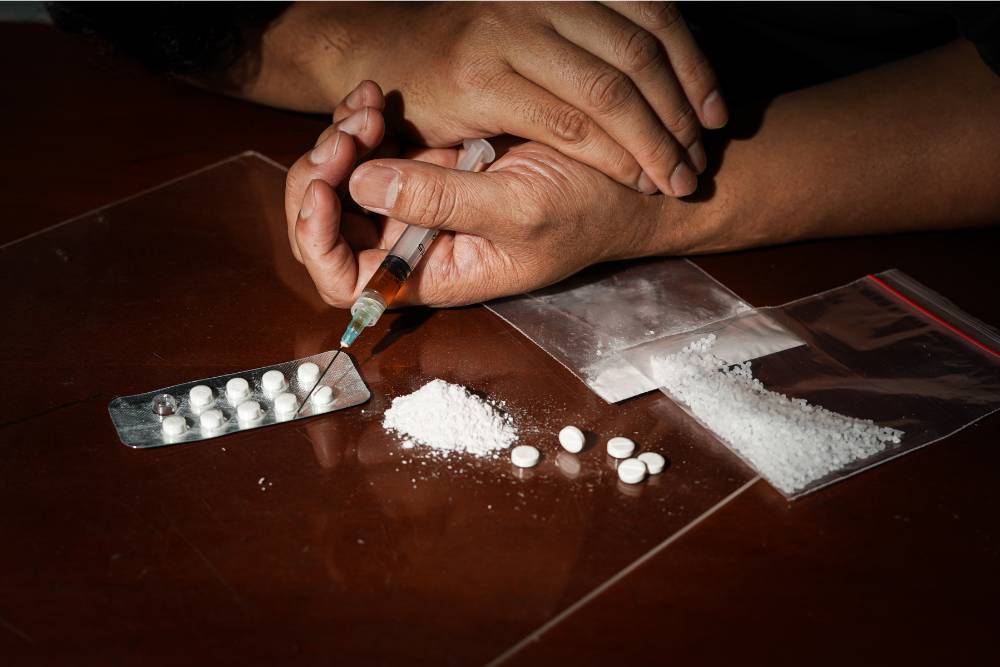Person preparing to inject drugs with various substances on the table, representing the need for effective meth addiction treatment in Huntington Beach, CA.