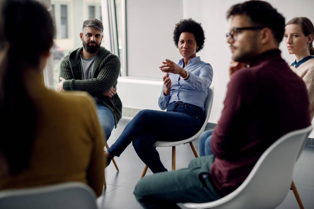 Group therapy session with diverse individuals seated in a circle, engaging in discussion as part of prescription drugs addiction treatment in Huntington Beach, CA.