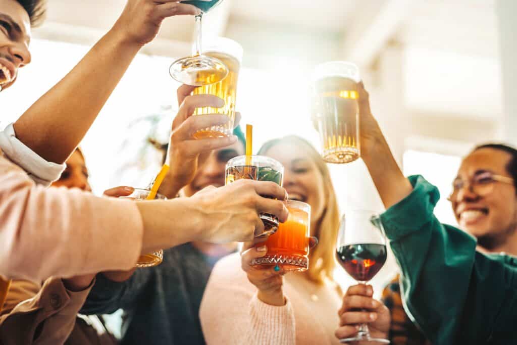 A group of young, active adults smiling and drinking beer and seltzers together at an outdoor party, illustrating the normalized drinking culture in Huntington Beach.